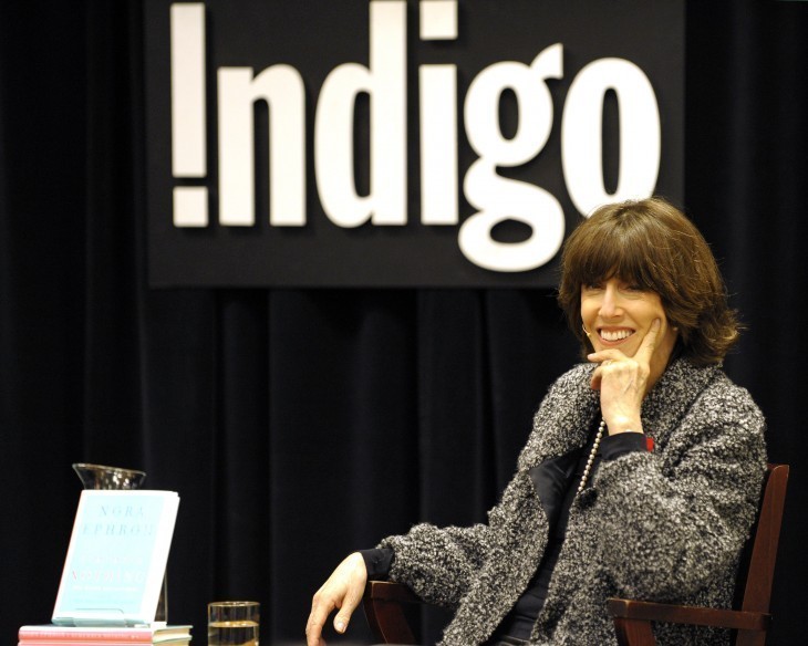 Photo of Nora Ephron smiling as she sits onstage at a presentation