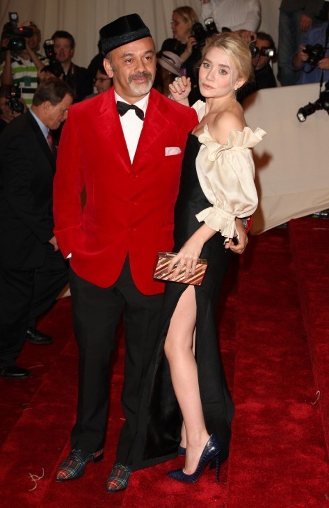 Photo of Ashley Olsen showing bare leg as she poses with a man in red tuxedo and a black velvit kefi or cap of some kind
