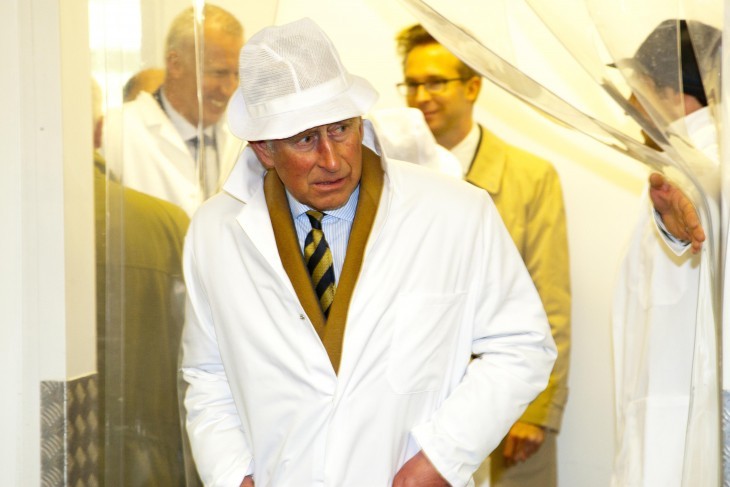 Photo of Prince Charles ducking through a plastic hanging door shield in a funny hairnet and white coat