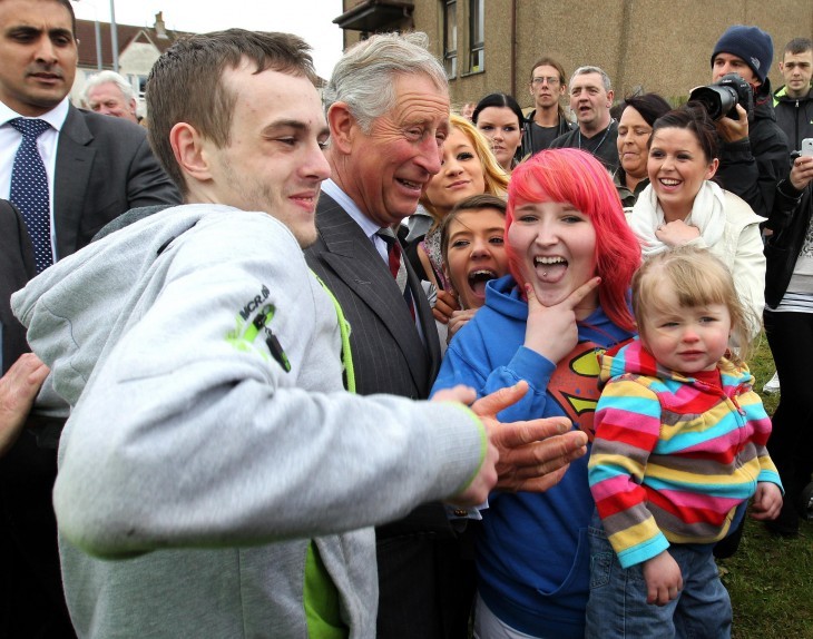 Photo of Prince Charles, laughing with a scruffy group of colorful local 20-somethings with rainbow hair and hoodies