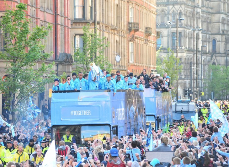 A bus loaded with Manchester City football players rolls through a crowd in a massive parade