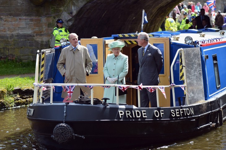 Photo of Prince Charles, Queen Elizabeth, and Prince Philip standing on the front of a canal barge as it goes under a low bridge
