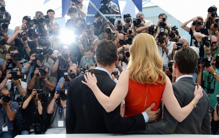 Photo of Nicole Kidman at Cannes, from behind, posing for a bank of photographers with her arms around two men
