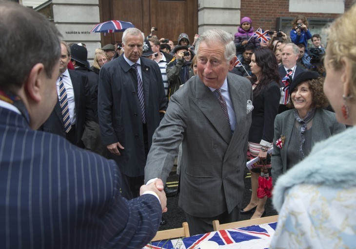 Photo of Prince Charles shaking the hand of a commoner, smiling just slightly, in a blue suit (the prince, that is)