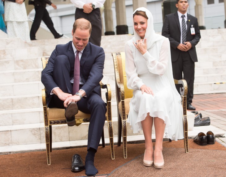 Photo of Prince William putting on a black dress shoe while Kate smiles beside him