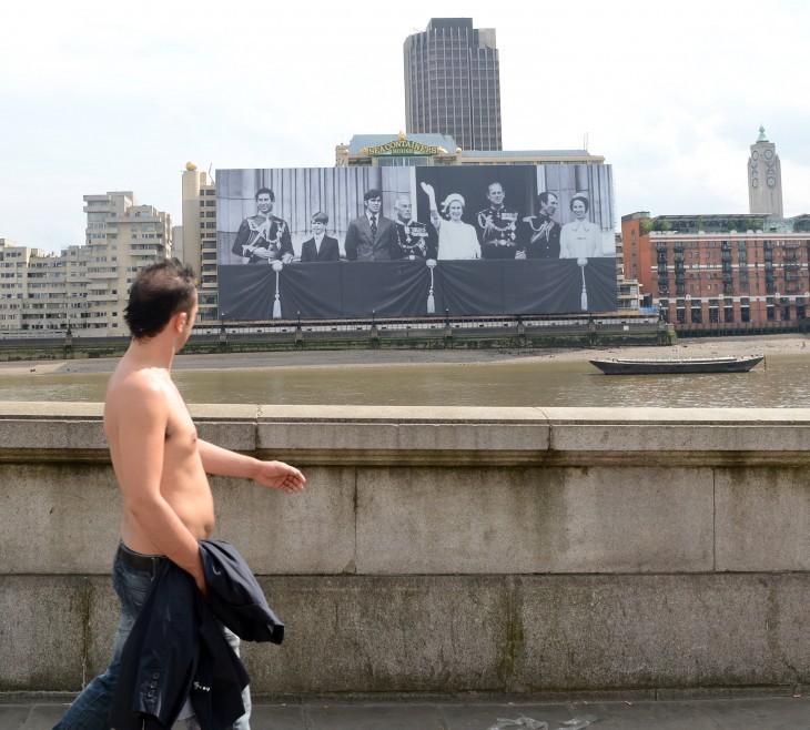 A topless man looks across the Thames at a huge photo of the Royal Family