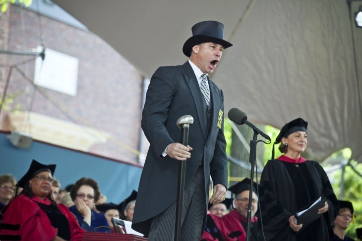 Photo of a sheriff in a top hat, banging a huge stick and shouting on the graduation stage