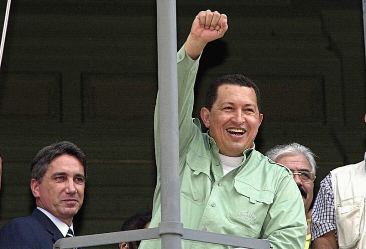 Photo of Hugo Chavez, in a mint-green shirt, raising a fist and smiling at a crowd