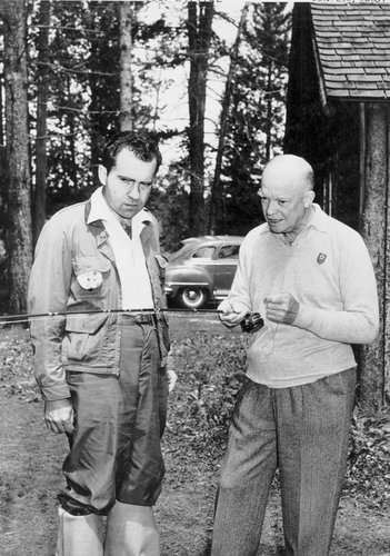 Photo of Dwight Eisenhower showing a fishing rod to Dick Nixon, who scowls at the lure in nutty rubber boots