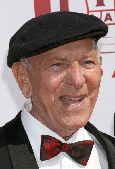 A photo of Jack Klugman in a bow tie and beret-type cap, grinning for cameras