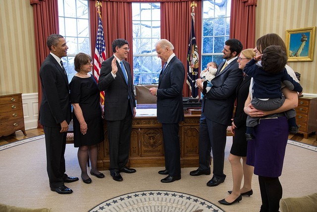 A photo of Jack Lew standing with hand raised in the Oval Office as family stands around 