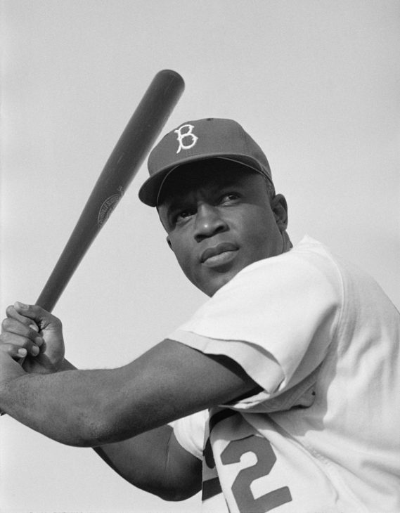 Photo of Jackie Robinson in Dodgers uniform, shot from below, poised to swing