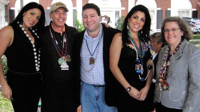 A party photo of five people on a lawn, smiling, wearing silly beads