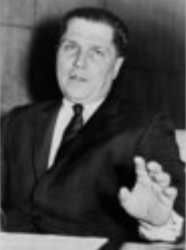 A photo of Jimmy Hoffa in a gray suit, smile-grimacing at camera as he raises a hand