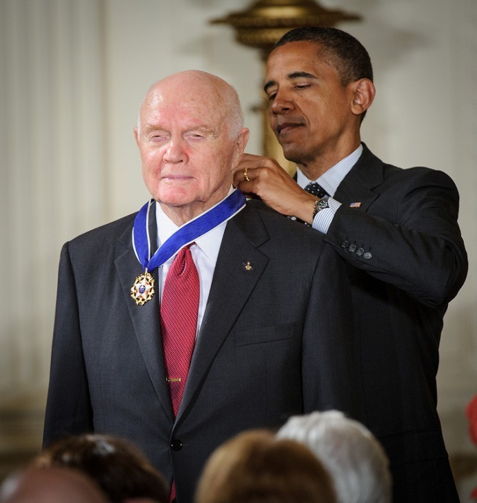 Photo of John Glenn standing proudly as Barack Obama drapes a fancy medal on a blue ribbon around his neck