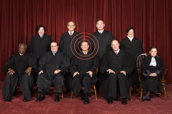 A photo of the U.S. Supreme Court, sitting formally in their robes, with a bulls-eye around the head of John Roberts