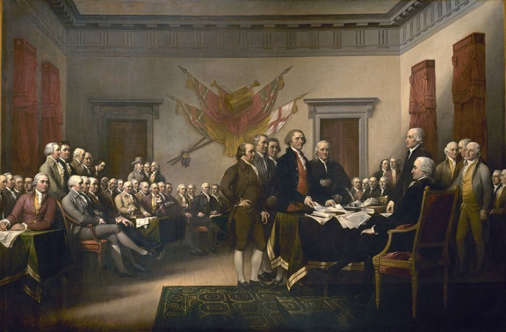 A painting of the Founding Fathers signing the Declaration of Independence in a big hall, all in fancy breeches and stockings