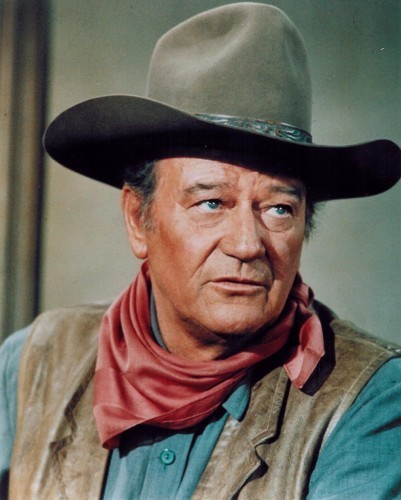 Photo of John Wayne in ten-gallon hat and neck scarf, looking rugged in a movie