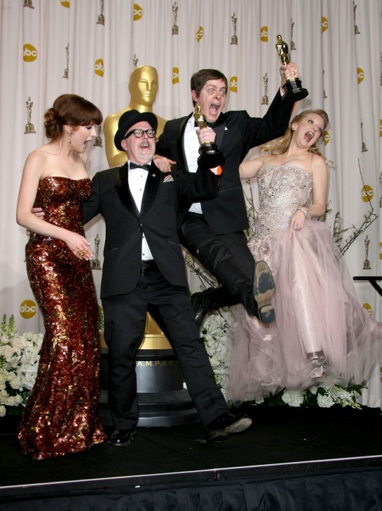 Four people in formal clothes and holding Oscars jump in the air