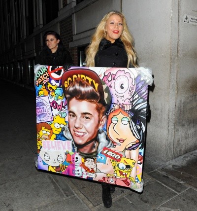 A youngish blonde Justin Bieber fan carries a weird painted collage of Bieber plus the Legos logo and scenes from 'Family Guy'