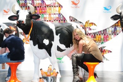 Kate Upton laughs as she sits with her hands under a plastic cow