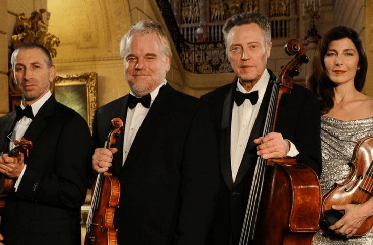 Four classical musicians lined up with their violins, smiling at the camera