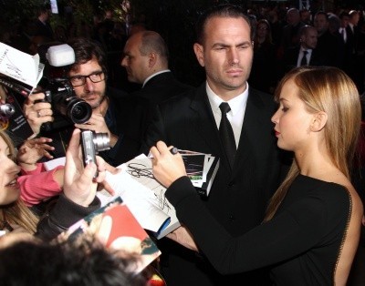 Photo of a bodyguard watching, scowling, as Jennifer Lawrence signs autographs for a crowd