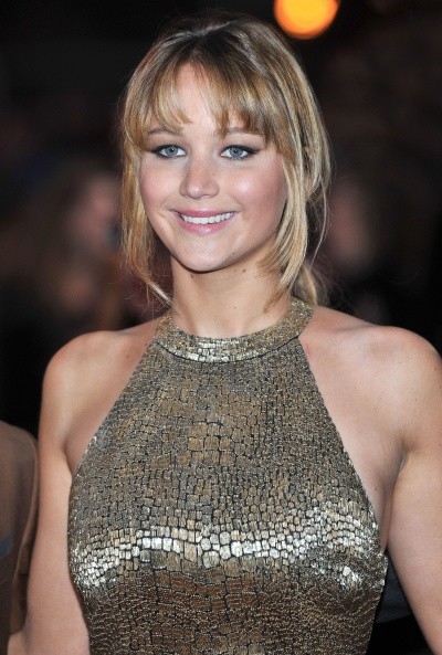 Photo of Jennifer Lawrence in a gold dress, smiling for cameras on the red carpet