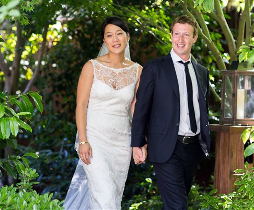 Photo of Mark Zuckerberg in a suit, with Priscilla Chan in a wedding dress, smiling among trees and plants