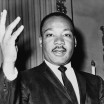 Photo of Martin Luther King, Jr. looking calmly straight at the camera with one hand oratorically upraised