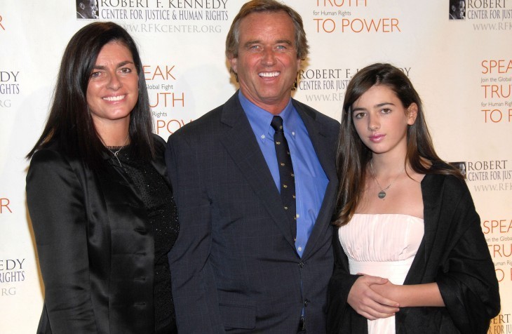 Mary Kennedy smiles for cameras with Robert Kennedy Jr. and a 13-year-oldish girl in front of a formal photo backdrop 