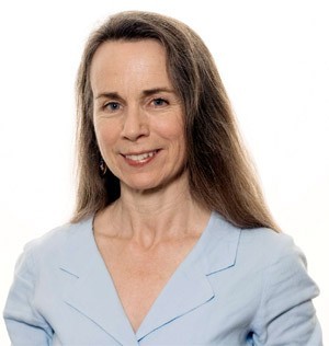 A photo of Mary Schmich, smiling, in a blue collared blouse, in a PR photo from her newspaper syndicate