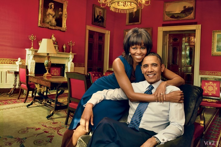 Michelle Obama hugs Barack as he sits in a chair and she leans over the back