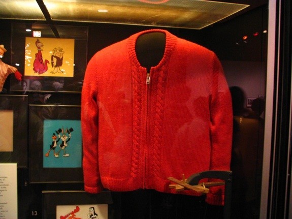 A photo of Mister Rogers red cardigan sweater hanging in a display case