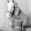 A woman stands smiling with a large tan horse