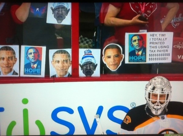 A photo of goalie Tim Thomas in front of a glass hockey rink wall plastered with Barack Obama posters