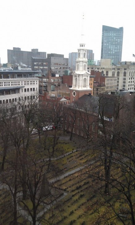 Fifth-floor photo of the Old Granary Burying Ground, with tombstones in a rainy row and the city skyline behind