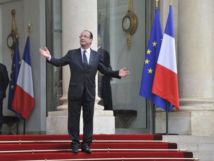 Francois Hollande smiles and raises his hands on the red carpet as if to say 