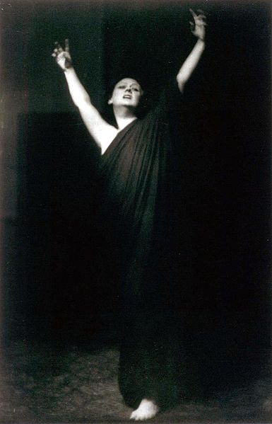 Photo of Isadora Duncan in a flowing gown, dancing, with arms held high