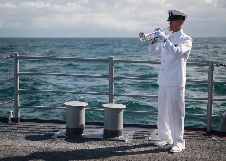 A sailor dressed in white plays a trumpet alone on a ship's deck