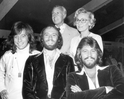 Three 30-ish Bee Gees brothers, smiling in front of their very parenty-looking silver-haired mum and dad