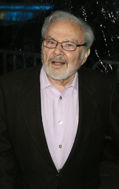 A photo of Maurice Sendak in a pink shirt and black vest, half-smiling outside a movie premiere