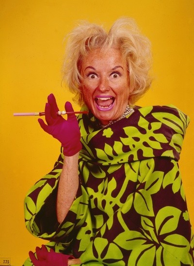 Photo of Phyllis Diller with a crazy flowered dress, wild hair, and an empty cigarette holder