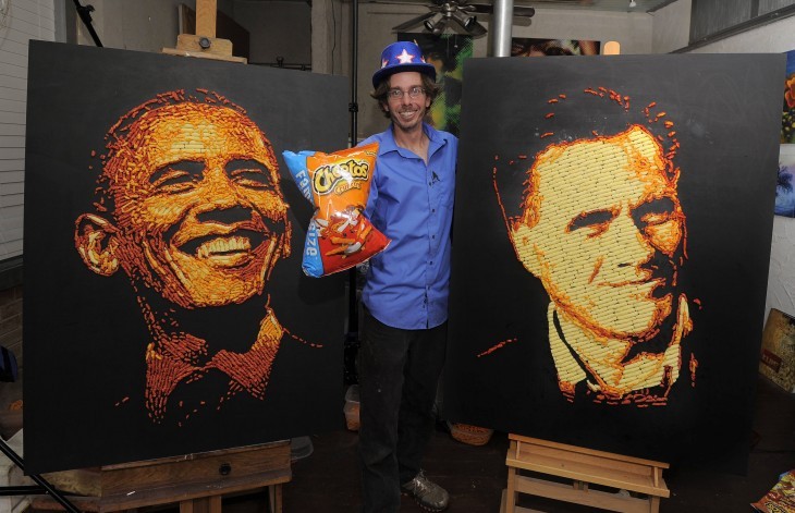 A smiling artist stands between two big portraits done in Cheetos