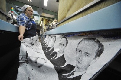 A worker woman holds a long sheet of photos of Vladimir Putin