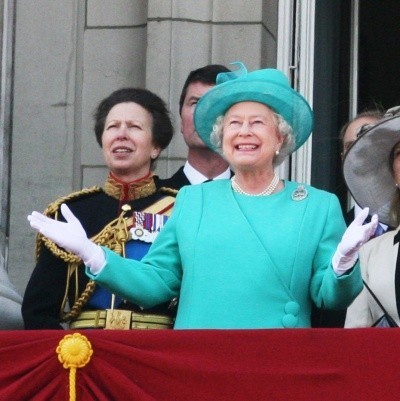 Photo of Queen Elizabeth in a bright aqua dress, surrounded by family, holding her hands up in delight
