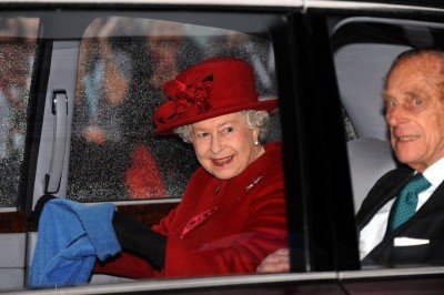 Photo of the queen and her consort in the back seat of a limo, smiling at crowds)