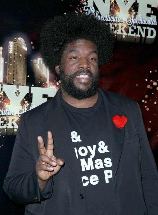 Questlove photo, with him in a black suit with a red heart and flashing the 'peace' sign