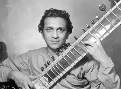 A photo of Ravi Shankar looking boldly at the camera with a sitar angled up in his lap