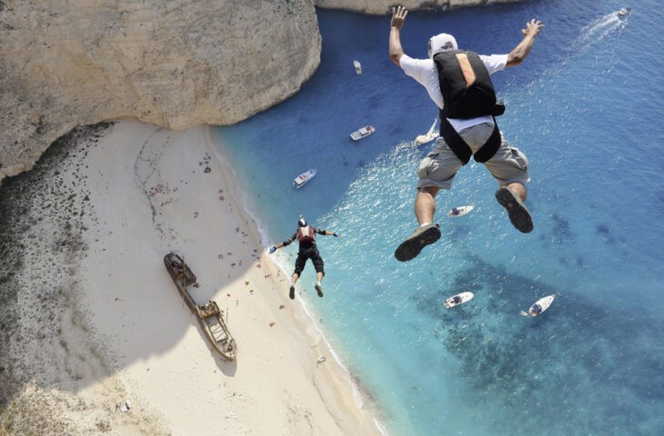 Two base jumpers plunge over the blue waters of a Greek beach